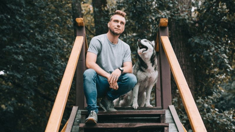 Man sitting on outdoor steps with a Siberian husky, both gazing into the distance.