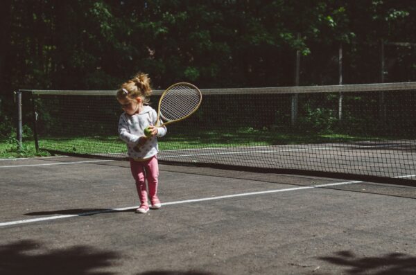 Young girl holding a tennis racket and ball on a tennis court.