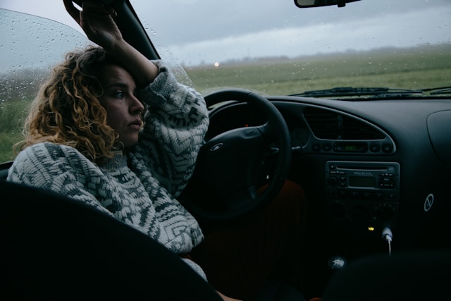 A thoughtful woman sitting in a parked car on a rainy day, thinking about the article she just read called Slip Out from the Chains of Overthinking: Practical Steps for Mental Clarity